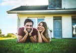 Casal feliz deitado na relva à porta de casa depois de renovar a casa com a ajuda da assistente do projeto da DECO PROteste.